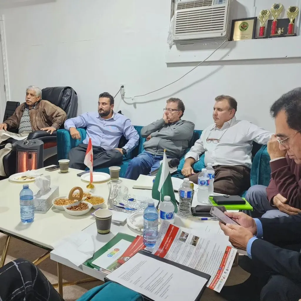 Board and advisory members seated around a table set with small Canadian and Pakistani flags